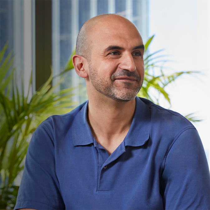 Ahmed sitzt drinnen. Er lächelt und schaut von der Kamera weg nach links.