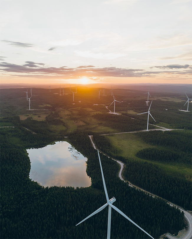 Mehrere energieproduzierende Windräder auf einer grünen Landschaft sind von oben zu sehen.