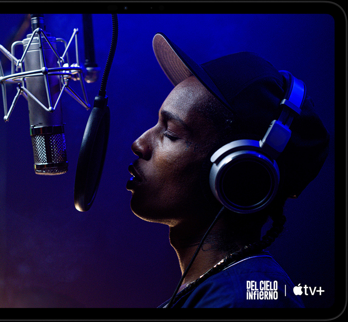 Un iPad Pro, posición horizontal, parte frontal, color negro espacial, esquinas redondeadas, marco de la pantalla negro, la pantalla muestra la app AppleTV+ reproduciendo una escena de una película de Apple TV+ Highest 2 Lowest con ASAP Rocky como Yung Felon rapeando frente a un micrófono