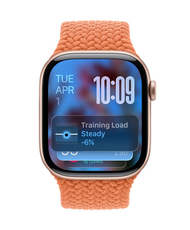 Apple Watch berwarna Emas Rose dengan tali jam rajutan berwarna Jingga Terang, wajah jam menunjukkan tanggal di kiri atas, waktu dengan susunan vertikal angka jam di kanan atas, widget Beban Latihan di bagian bawah, semuanya dalam Liquid Glass tembus pandang