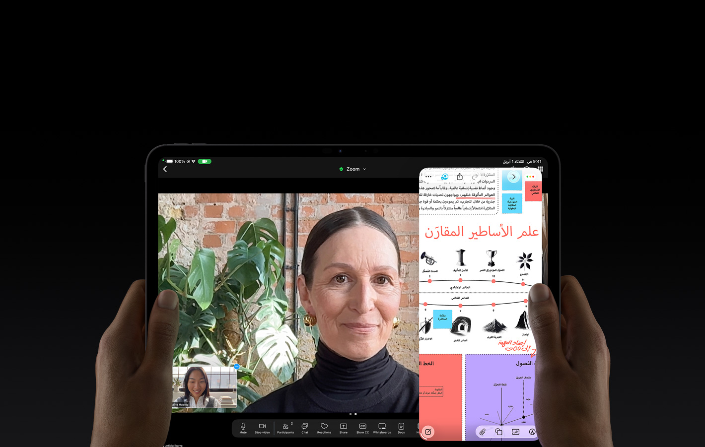 جهاز iPad Pro، الجزء الأمامي الخارجي، لون أسود فلكي، يدان يسرى ويمنى تحملان الجهاز في الوضع الأفقي، زوايا مدورة، إطار شاشة أسود، واجهة تعرض محادثة فيس تايم تُترجم مباشرةً، وتطبيق تعليمي يُظهر عرضاً تقديمياً عن 
