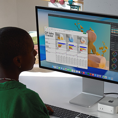 Woman working on an Excel spreadsheet on a Mac, sitting at a work table. The Excel spreadsheet is a Q4 sales tracker. Behind the Excel spreadsheet window is a Pixelmator Pro window.