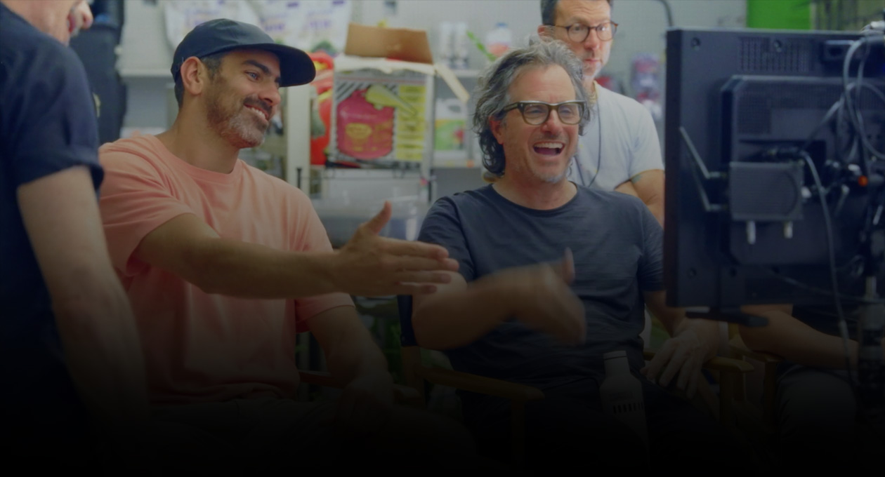 Kép két egymás mellett ülő filmesről, akik egy kivetítőre figyelnek és mutatnak.