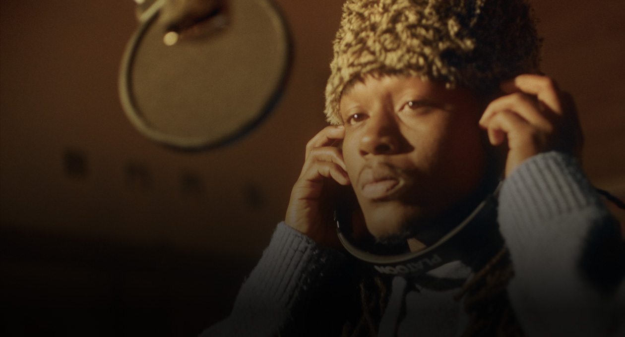 Fotó, melyen Kiddo K egy zenestúdióban áll egy mikrofon előtt, és hallgatja, ami a fejhallgatójából szól