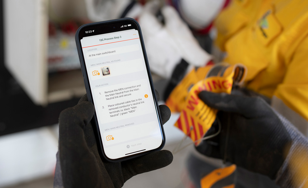 Zwei Hände halten ein iPhone, das auf dem Bildschirm die Anweisung „13C Process Step 3“ zur Durchführung eines Schalttafeltests anzeigt