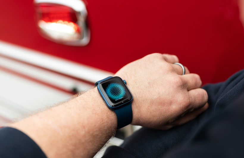 Une Apple Watch portée au poignet affiche le message: Maintenant, inspirez, avec un camion de pompiers à proximité