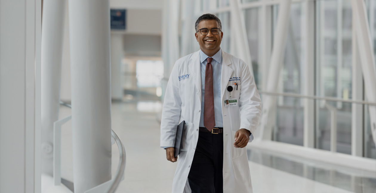 Un médecin marche en tenant un MacBook sous son bras droit.