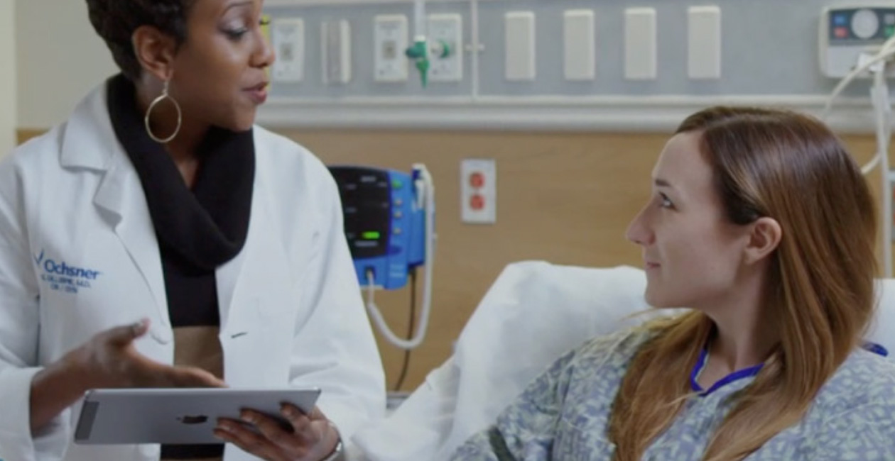 Un prestataire de soins muni d’un iPad s’adresse à une personne dans un lit d’hôpital.