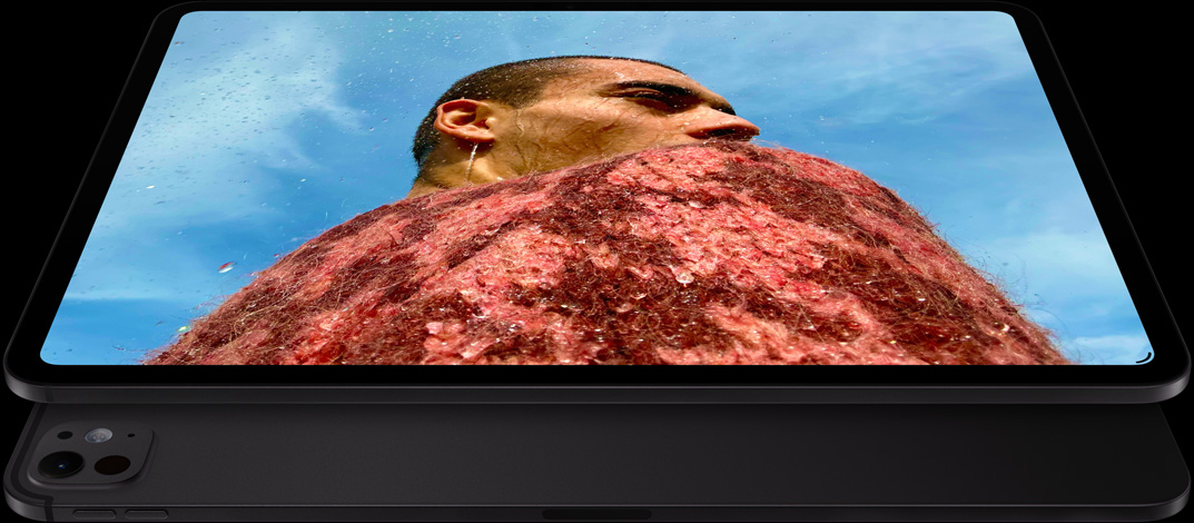 iPad Pro, priekšpuses skats, horizontāls novietojums, astromelna krāsa, noapaļoti stūri, melns displeja ietvars, displejā bilde, kurā ir vīrietis sarkanā džemperī un zilas debesis, apakšā vēl viens iPad Pro, aizmugures skats, horizontāls novietojums, astromelna krāsa, pro kameru sistēma, skaļuma palielināšanas poga, skaļuma samazināšanas poga