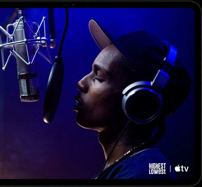 iPad Pro, horizontāls novietojums, priekšpuses skats, astromelna krāsa, noapaļoti stūri, melns displeja ietvars, displejā tiek rādīts, kā AppleTV+ demonstrē ainu no Apple TV+ oriģinālās filmas Highest 2 Lowest ar ASAP Rocky, kurš Yung Felon lomā repo mikrofonā