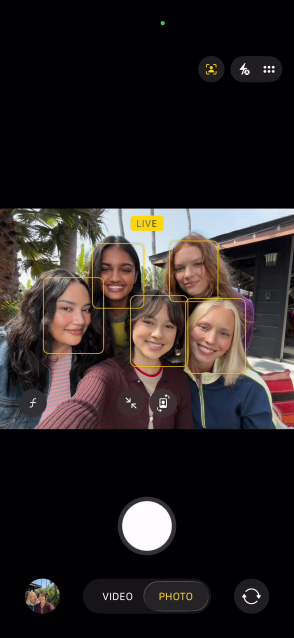 iPhone 17 priekšējais ekrāns, kurā redzams grupas selfijs ar Center Stage fotografēšanas funkciju