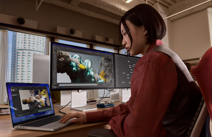 Dans un bureau, une personne travaille sur un MacBook Pro connecté à un Studio Display XDR