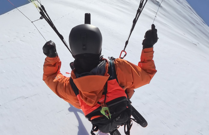 Une personne faisant du paraski dans les airs au-dessus d’une montagne en plan large