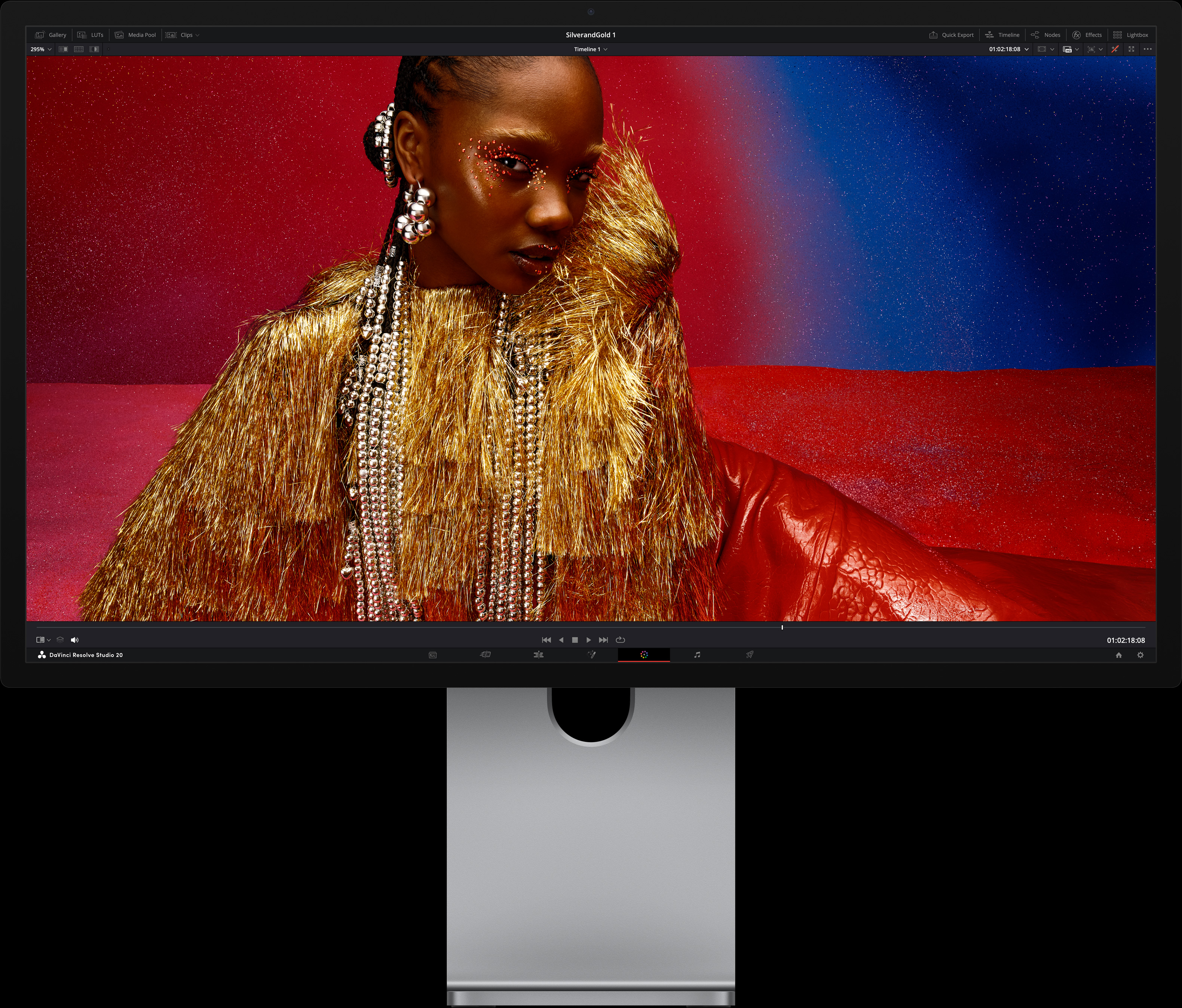 Sēdošai personai, kas ir tērpusies spilgti sarkanā kleitā un uzlikusi lielus metāliskus aksesuārus, fonā ir zila un sarkana krāsu pāreja, parādot Studio Display XDR attēla kvalitāti