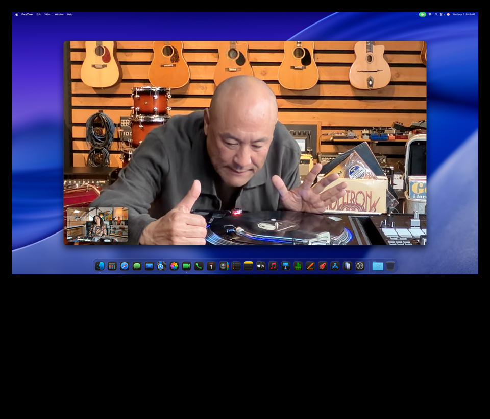 在 Studio Display XDR 上進行視訊通話時，Mac Studio 收納在下方，樂器行的人湊近了看黑膠唱片機。